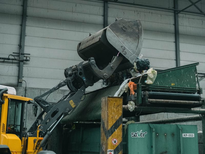 Shovel kiept afval uit zijn bak op een transportband in een afvalverwerkingshal