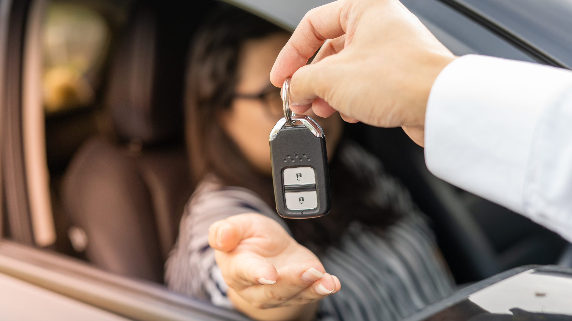 Medewerker geeft een autosleutel aan een bestuurder door het open zijraam