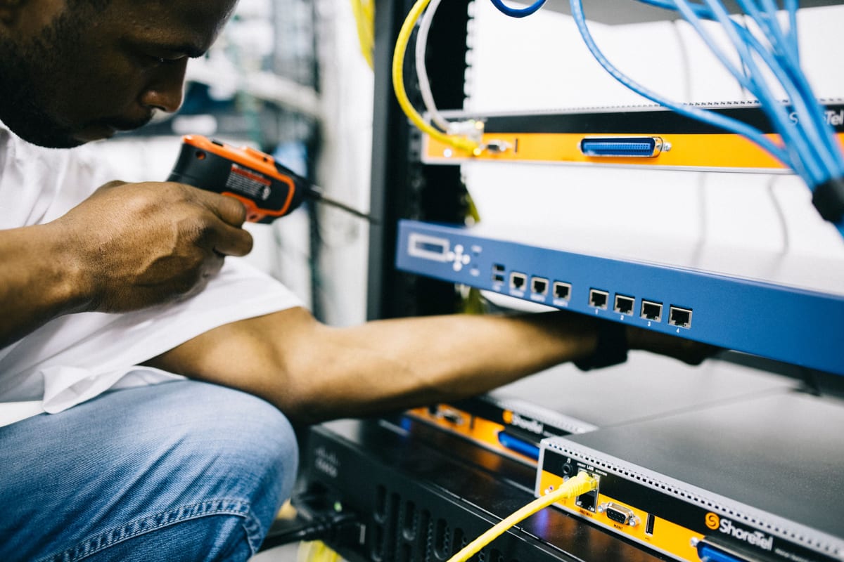 Installateur schroeft een netwerkswitch vast in een patchkast met blauwe en gele kabels