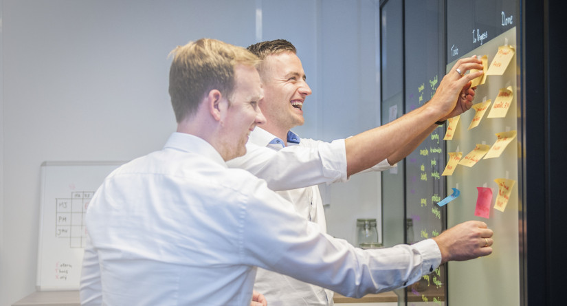 Twee Jump-collega's plakken post-its op een glazen wand